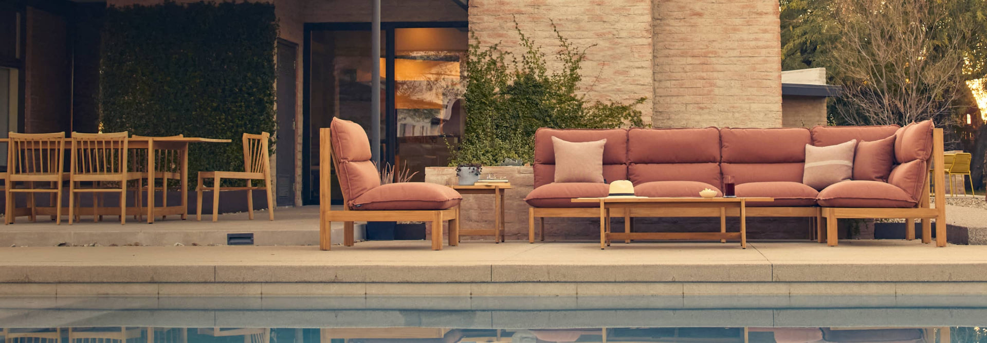 Neighbor Teak sectional with rust-colored cushions with coffee table and chairs on pool deck against a modern home