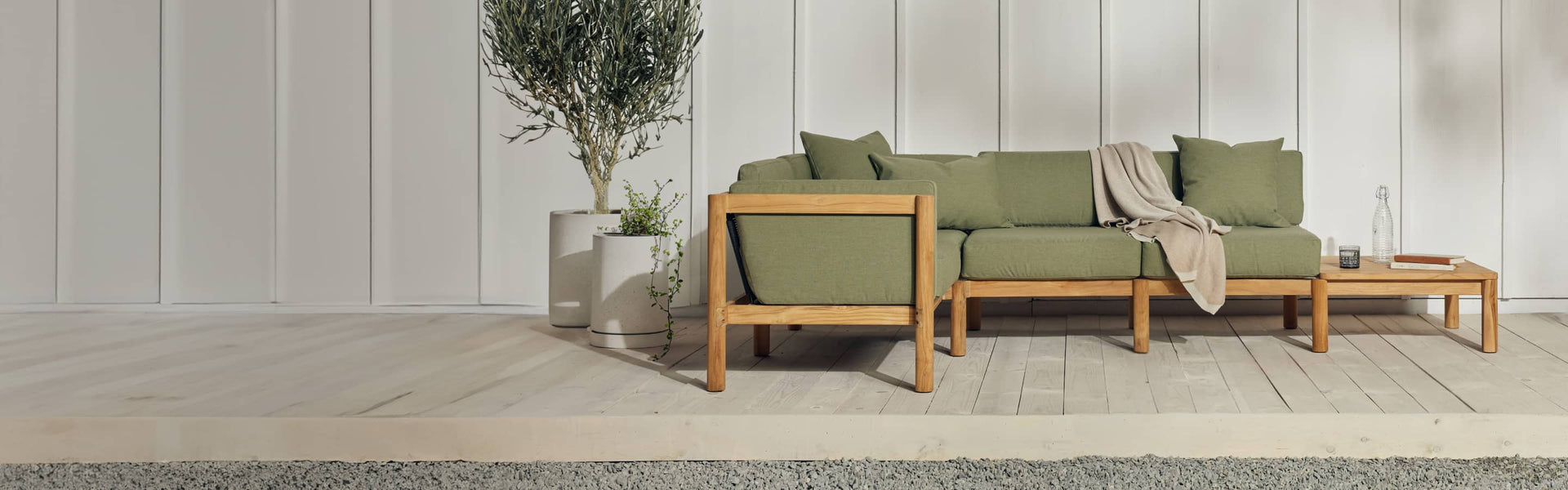 Neighbor teak outdoor sectional with an end table on a patio with a potted olive tree