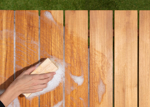 Woman's hand with bristled brush cleaning teak table with soap