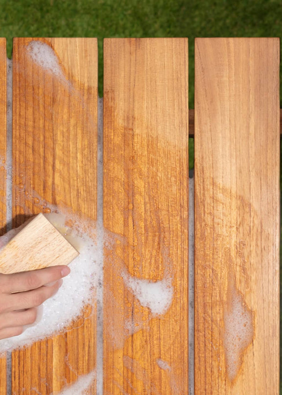 Woman's hand with bristled brush cleaning teak table with soap