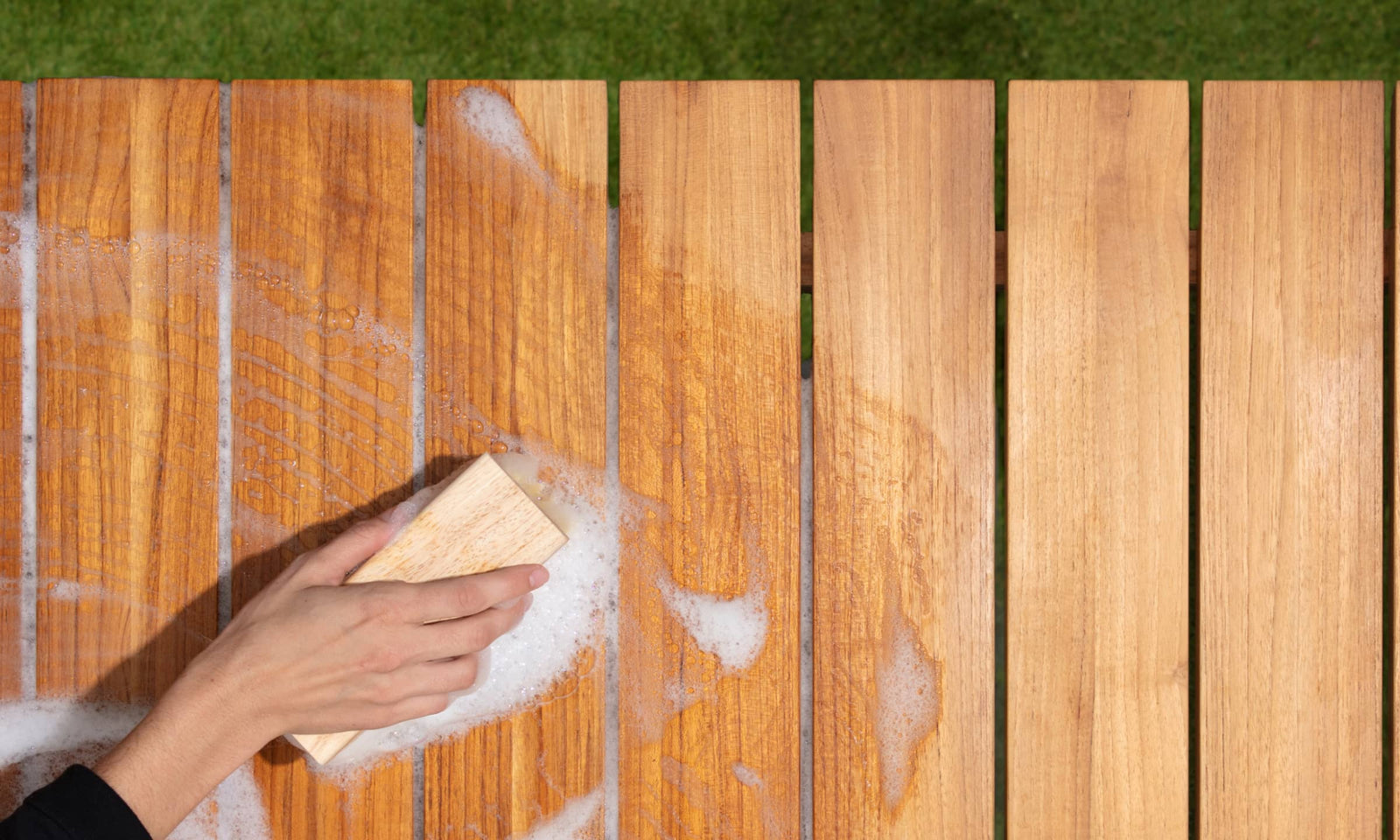 Woman's hand with bristled brush cleaning teak table with soap