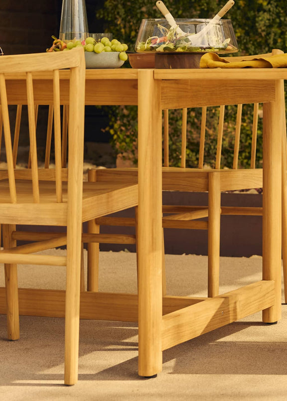 teak outdoor dining table with woman's body in motion in foreground