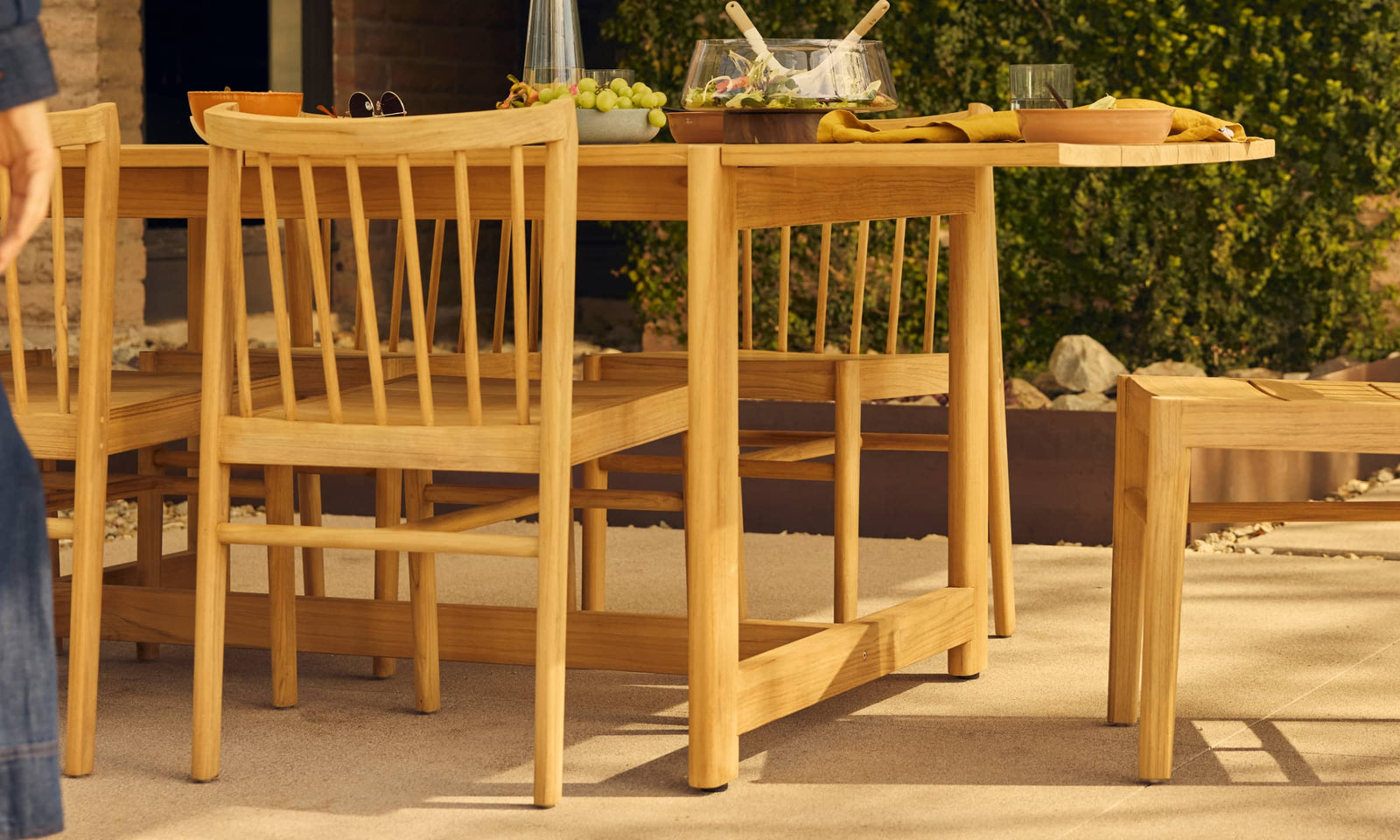 teak outdoor dining table with woman's body in motion in foreground