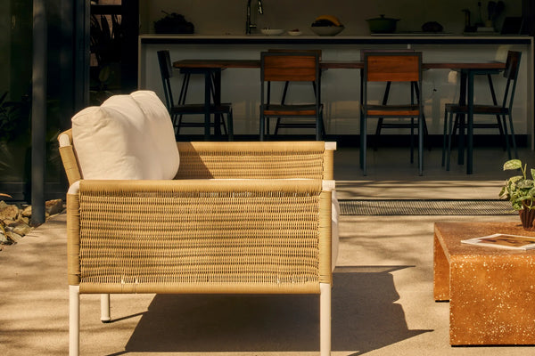 Rattan outdoor sofa with white cushions in a sunny backyard