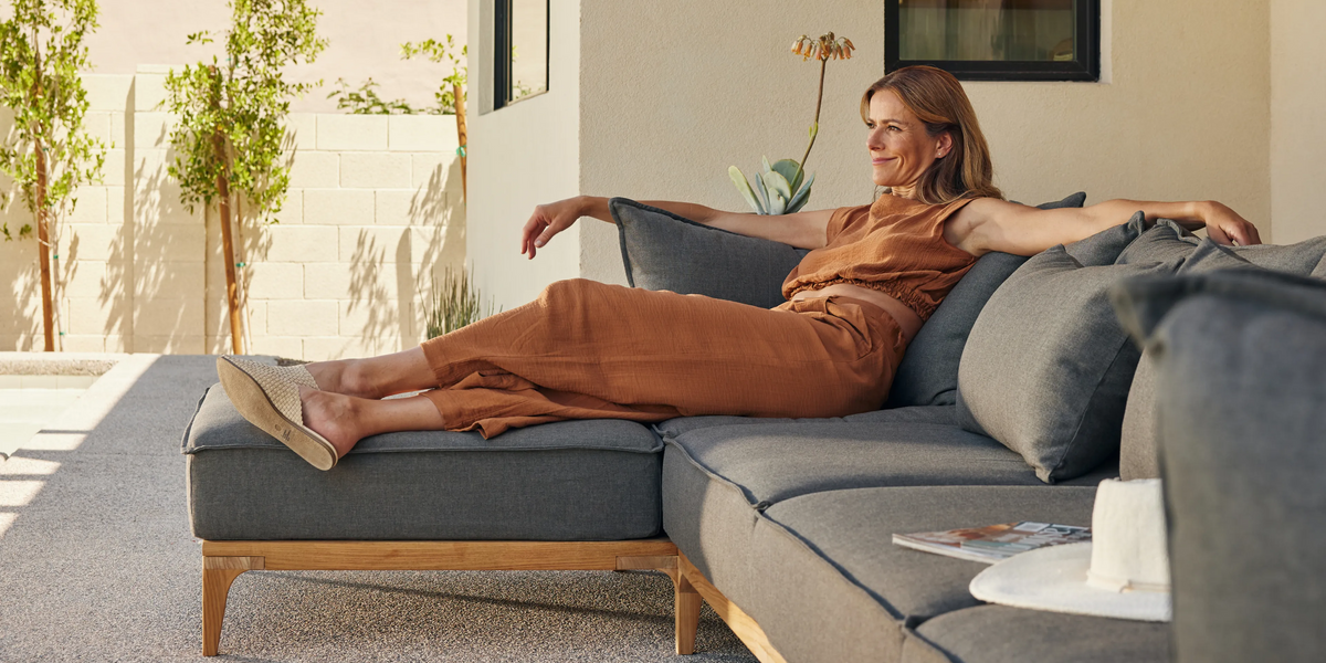 Woman lounging outside on a grey upholstered teak outdoor sectional
