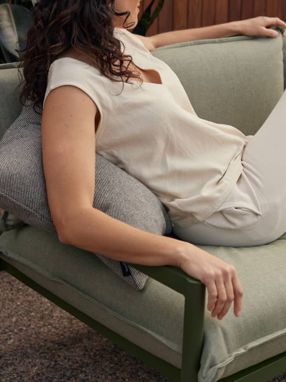 Woman lounging on outdoor green upholstered sofa