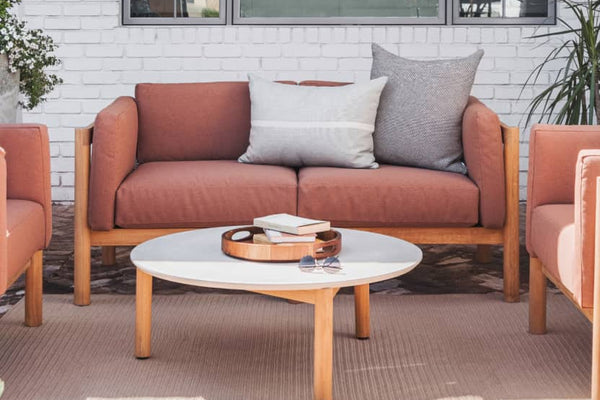 Rust colored upholstered loveseat with plush pillows on top of it