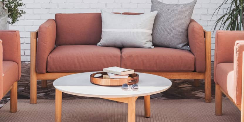 Rust colored upholstered loveseat with plush pillows on top of it