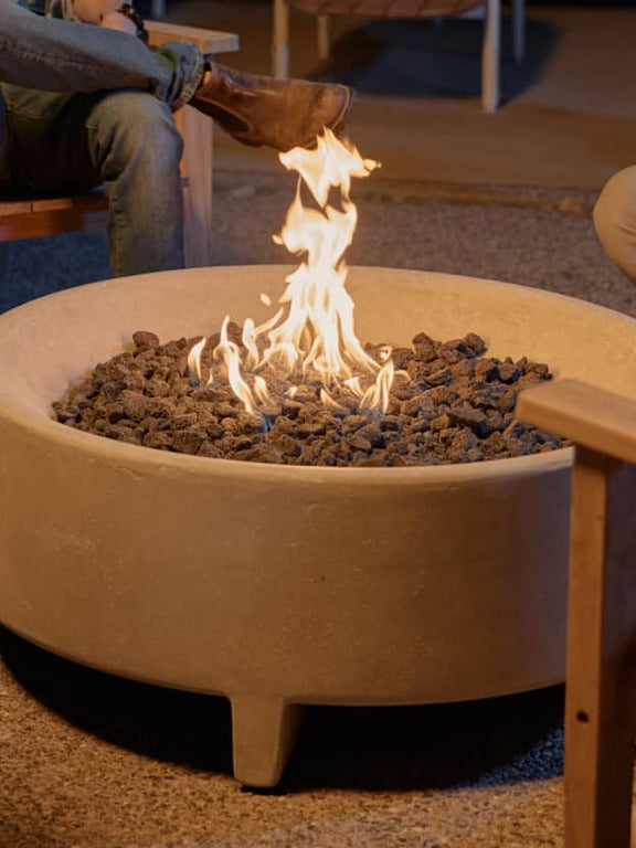 Neighbor round concrete fire pit table in a backyard surrounded by friends sat in teak Adirondack chairs