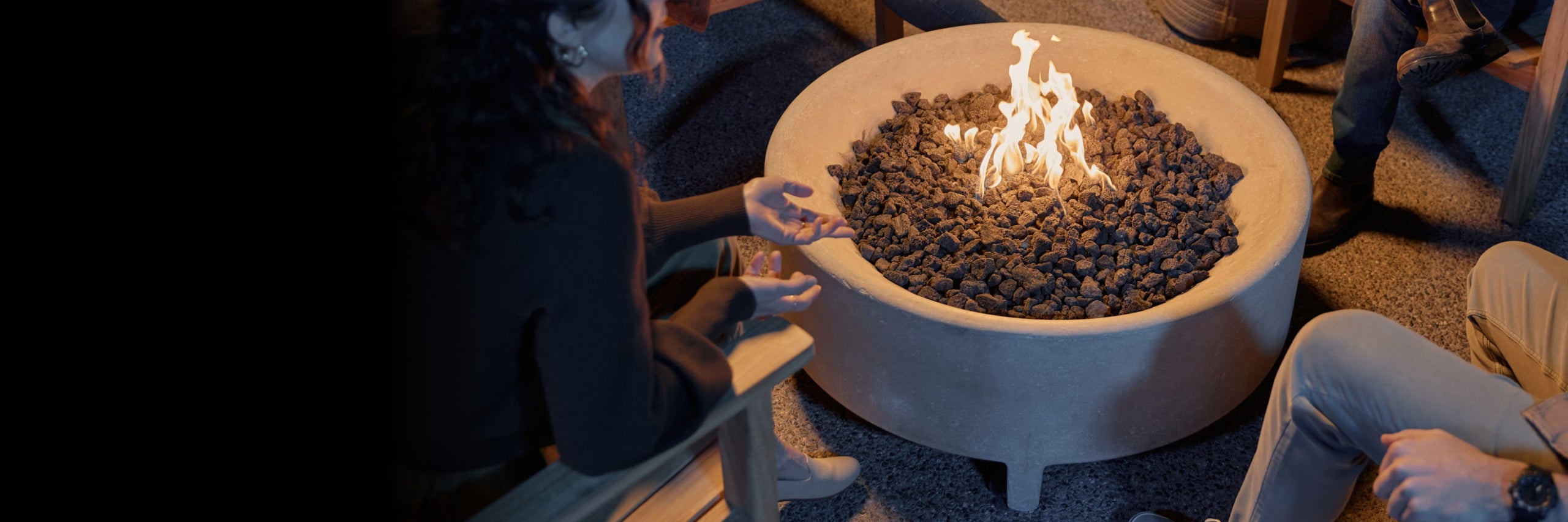 People gathered around a fire pit table with flames in a dimly lit patio