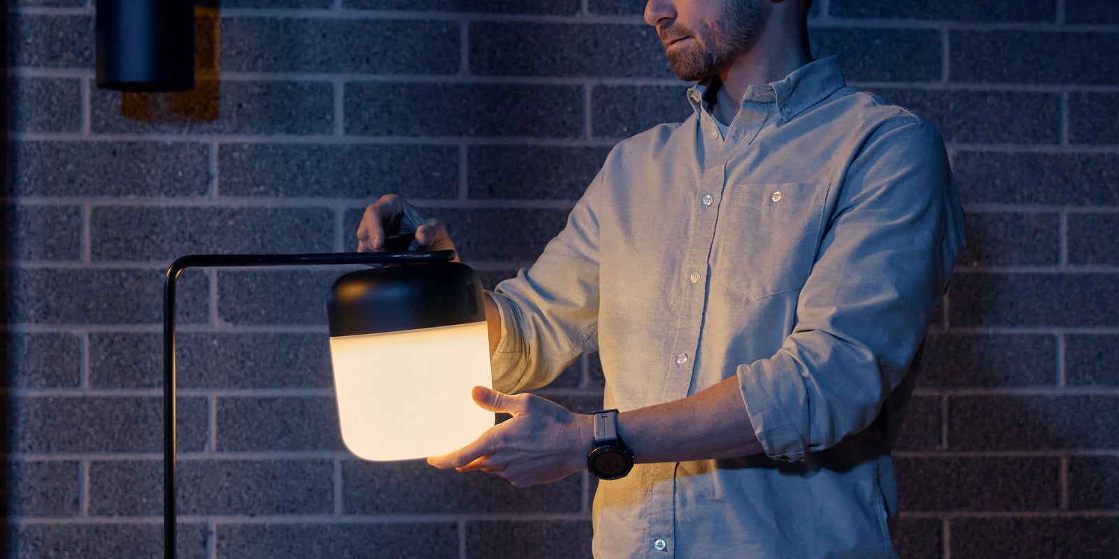 Man attaching Neighbor Acorn Lantern to the Acorn Stand against a brick exterior wall at dusk