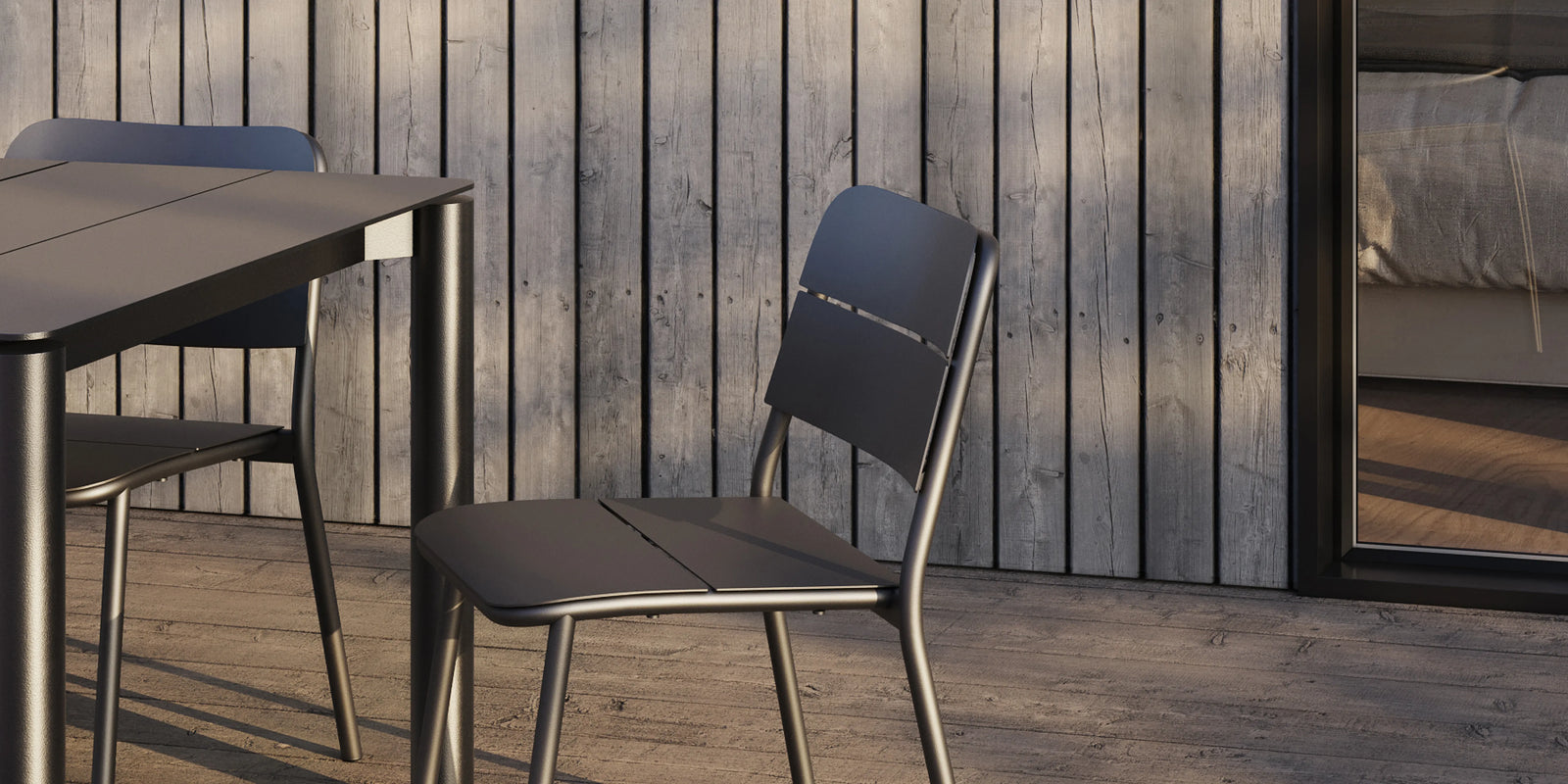 Neighbor Bandwidth Dining Chair in Charcoal beside matching table on a weathered wood deck with wood-slat wall backdrop