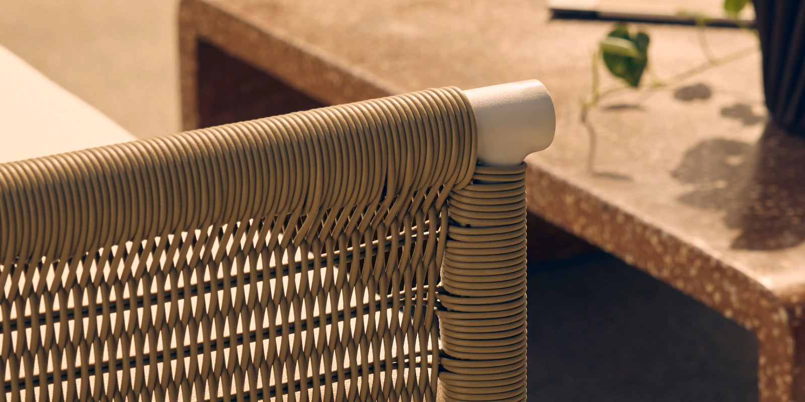 Neighbor Camber Chair with natural wicker weave and cream cushion in sunny outdoor setting with desert plants