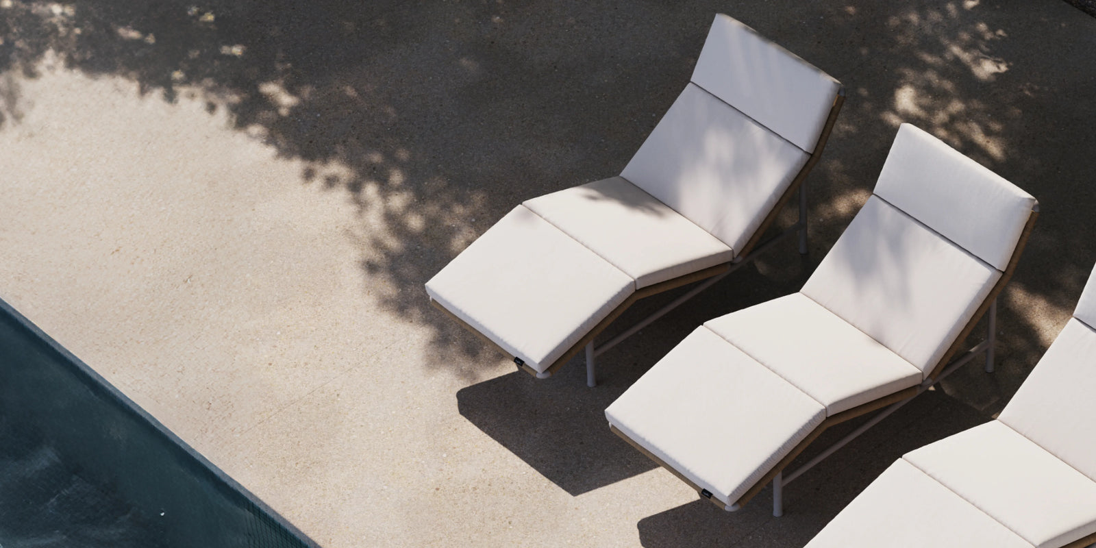 Two Neighbor Camber Chaise Lounge Chairs with cream cushions on concrete terrace beside a pool, aerial view