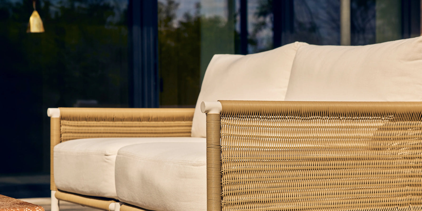 Neighbor Camber Loveseat with natural wicker frame and cream cushions on a sunlit outdoor patio