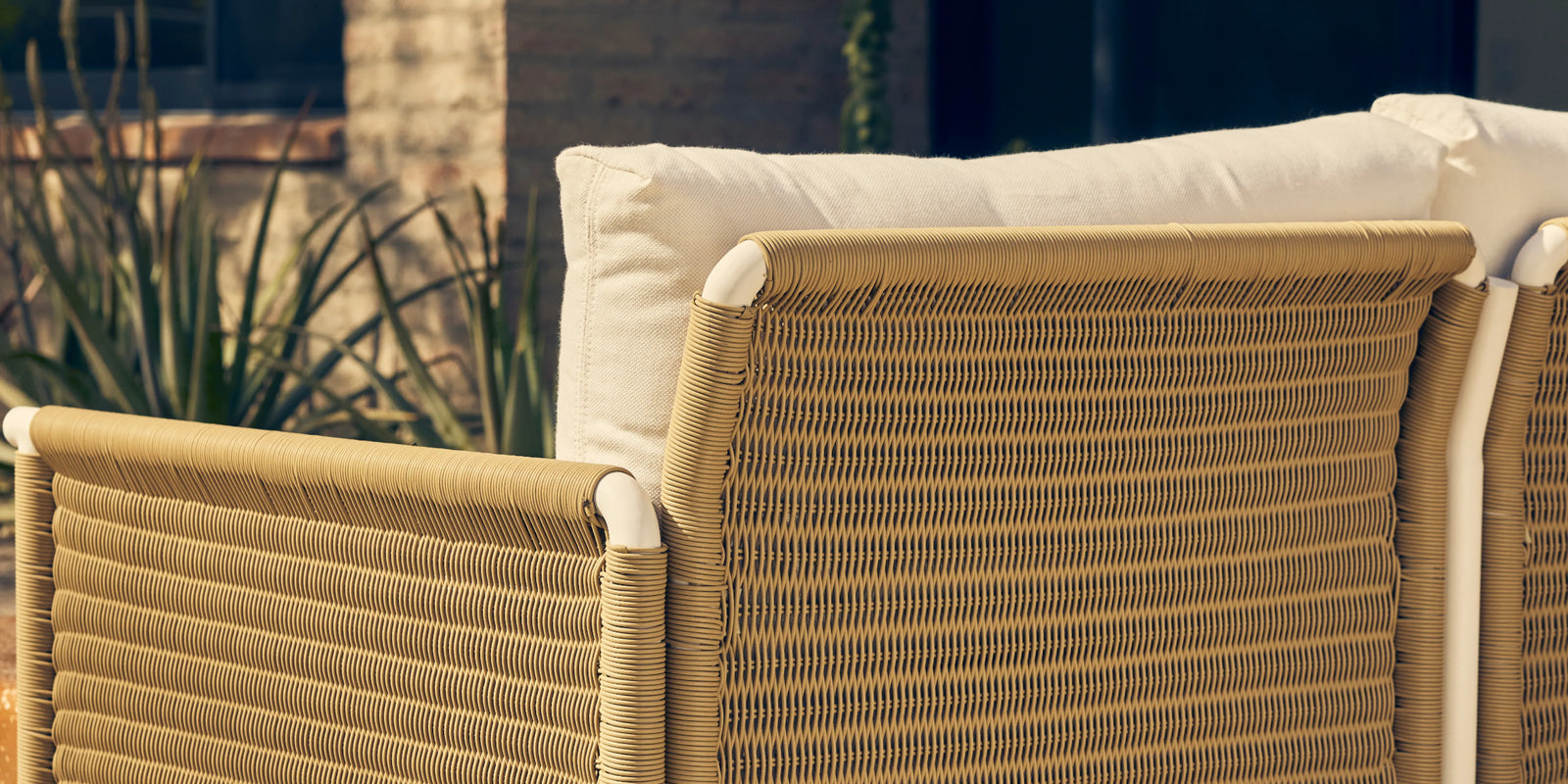 Neighbor Camber Sectional with natural wicker frame and cream cushions arranged on a sunlit terrace