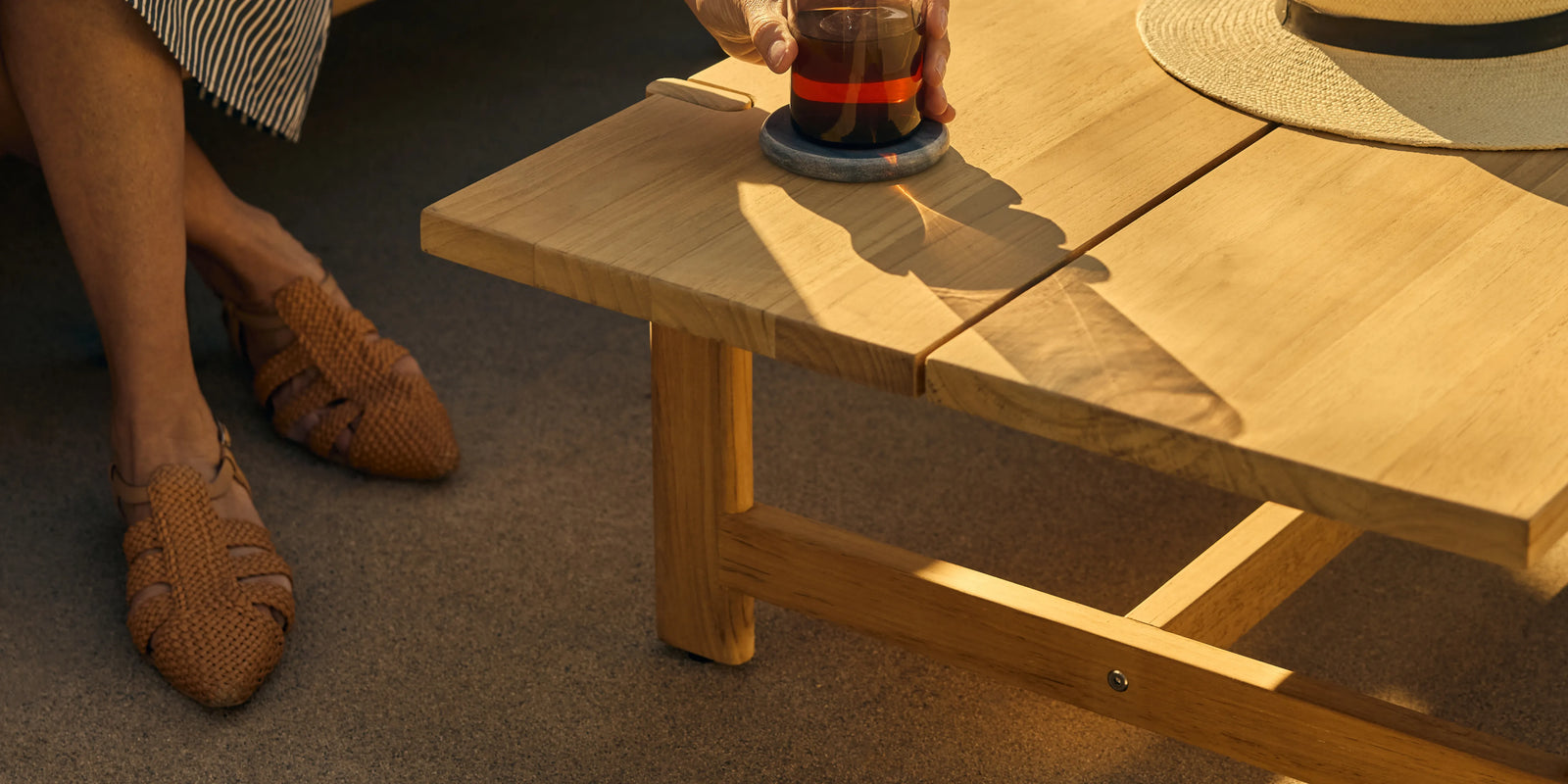 Neighbor Felloe Coffee Table in teak on outdoor patio with warm light and surrounding seating