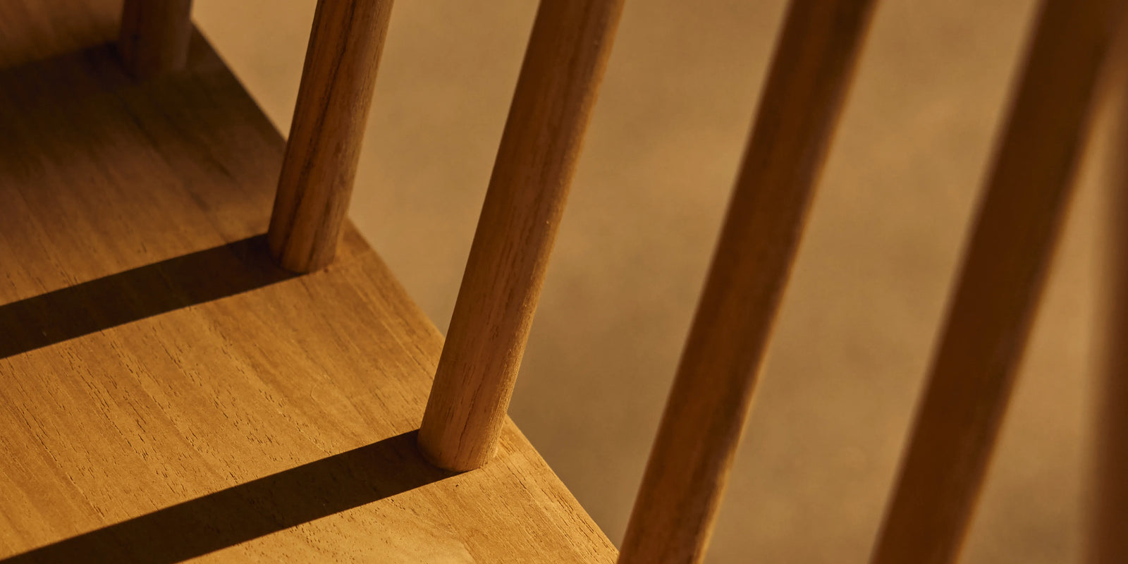Closeup of Neighbor Felloe Dining Chair back spindles casting shadows on teak seat in raking afternoon light