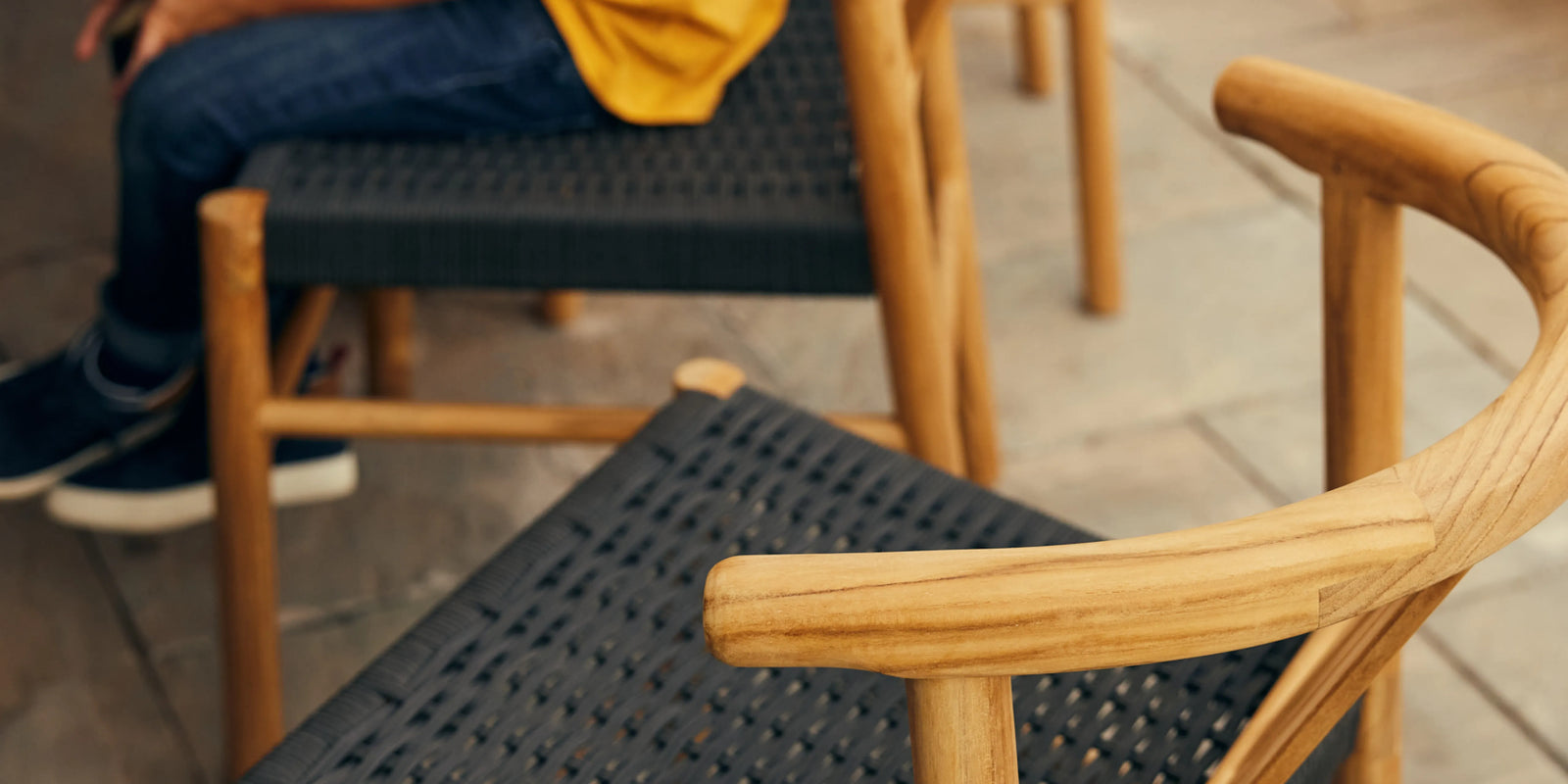 Closeup of Neighbor Haven Dining Chair teak arm and woven black seat with child seated in background
