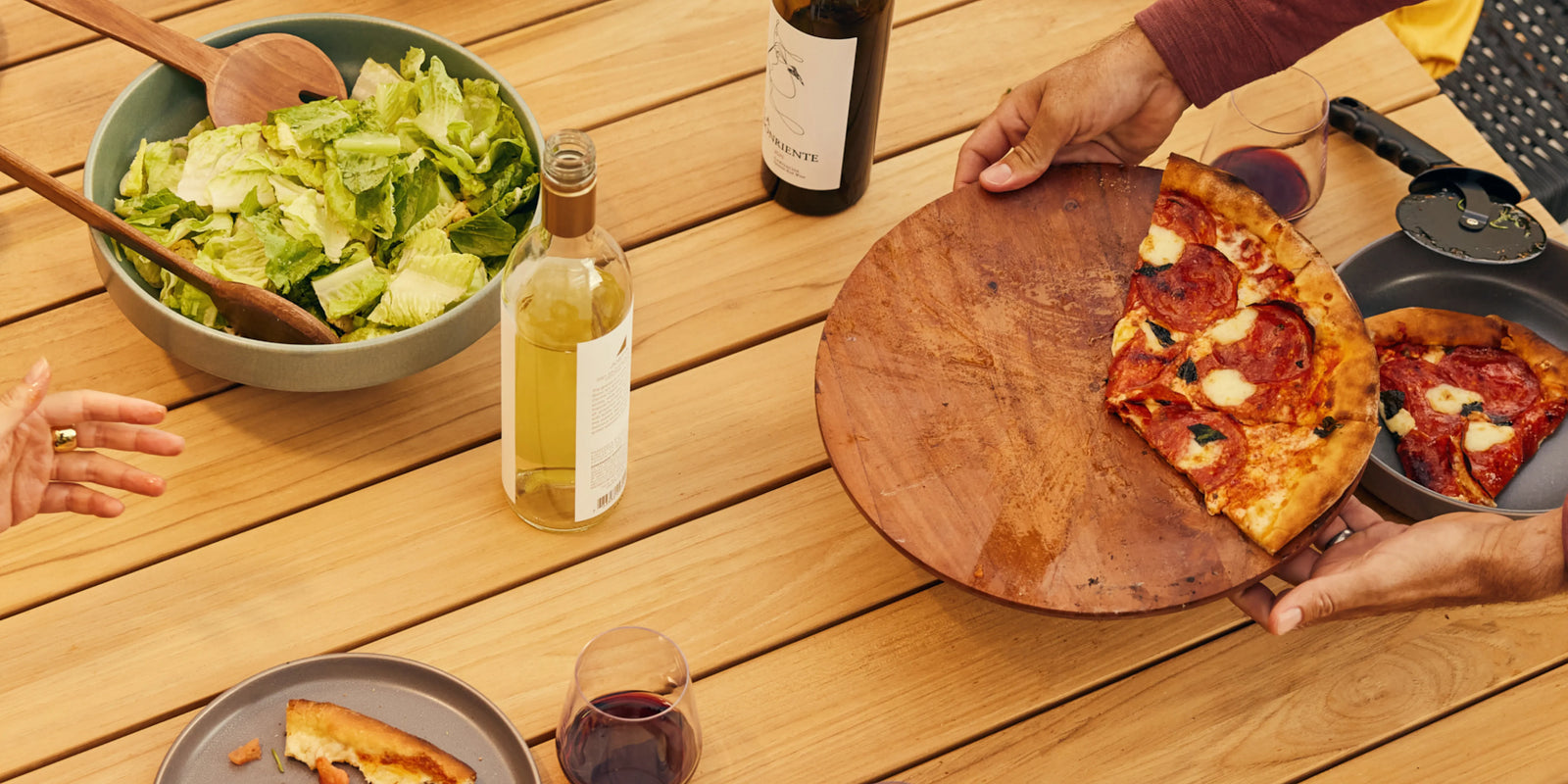 Closeup of Neighbor Haven Dining Table teak surface with chairs and gathered guests in background