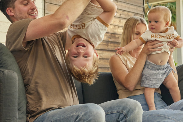 Family playing together on Neighbor Haven Loveseat in charcoal fabric with teak frame on a backyard patio