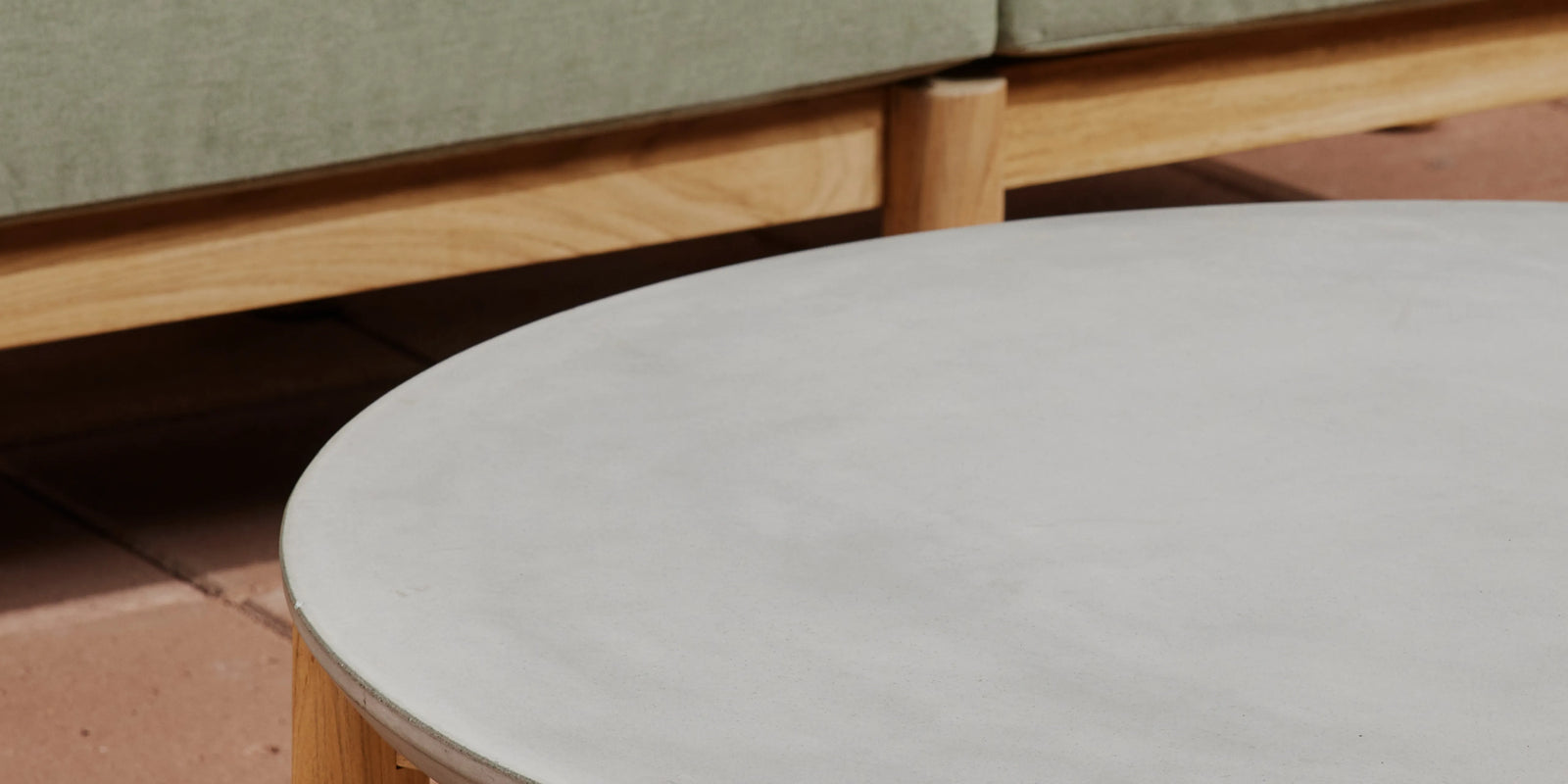 Closeup of Neighbor Haven Round Coffee Table concrete top with teak sofa base and brick tile floor behind