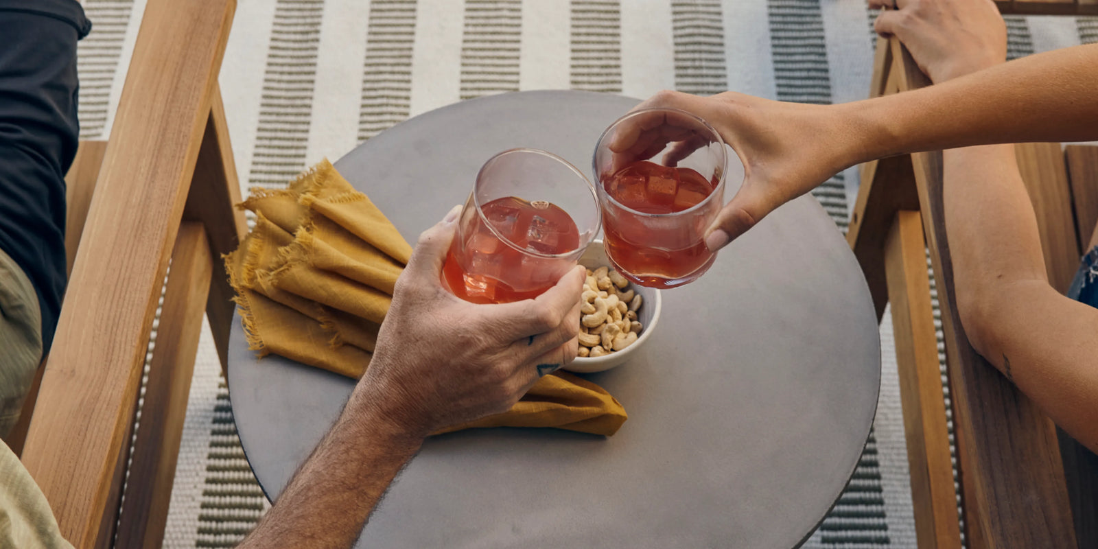 Two people clinking drinks over Neighbor Haven Side Table with concrete top on a striped outdoor rug