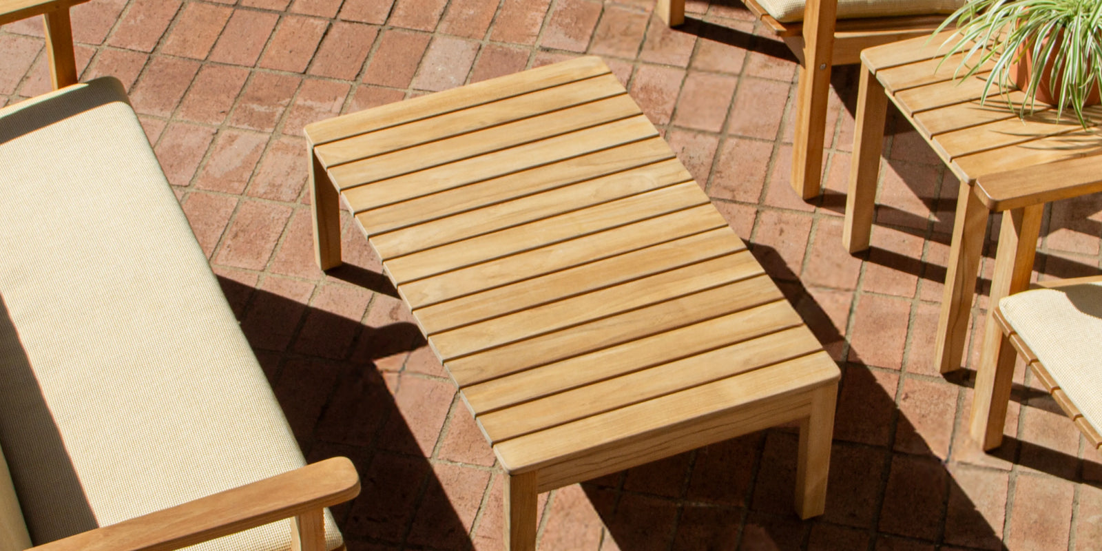 Overhead view of Neighbor Low Bench Pad with cream cushion on teak bench, matching chairs on terracotta tile patio