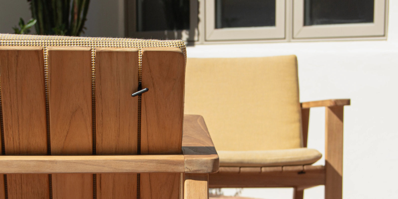 Closeup of Neighbor Low Bench Pad cream cushion on teak bench in afternoon sun on terracotta tile patio