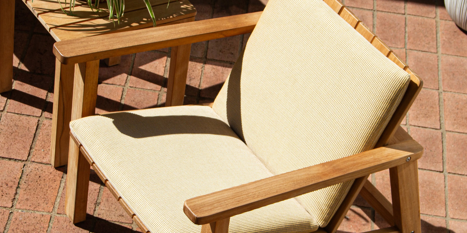 Neighbor Low Chair with cream cushion pad on teak frame on a terracotta tile patio in bright sun
