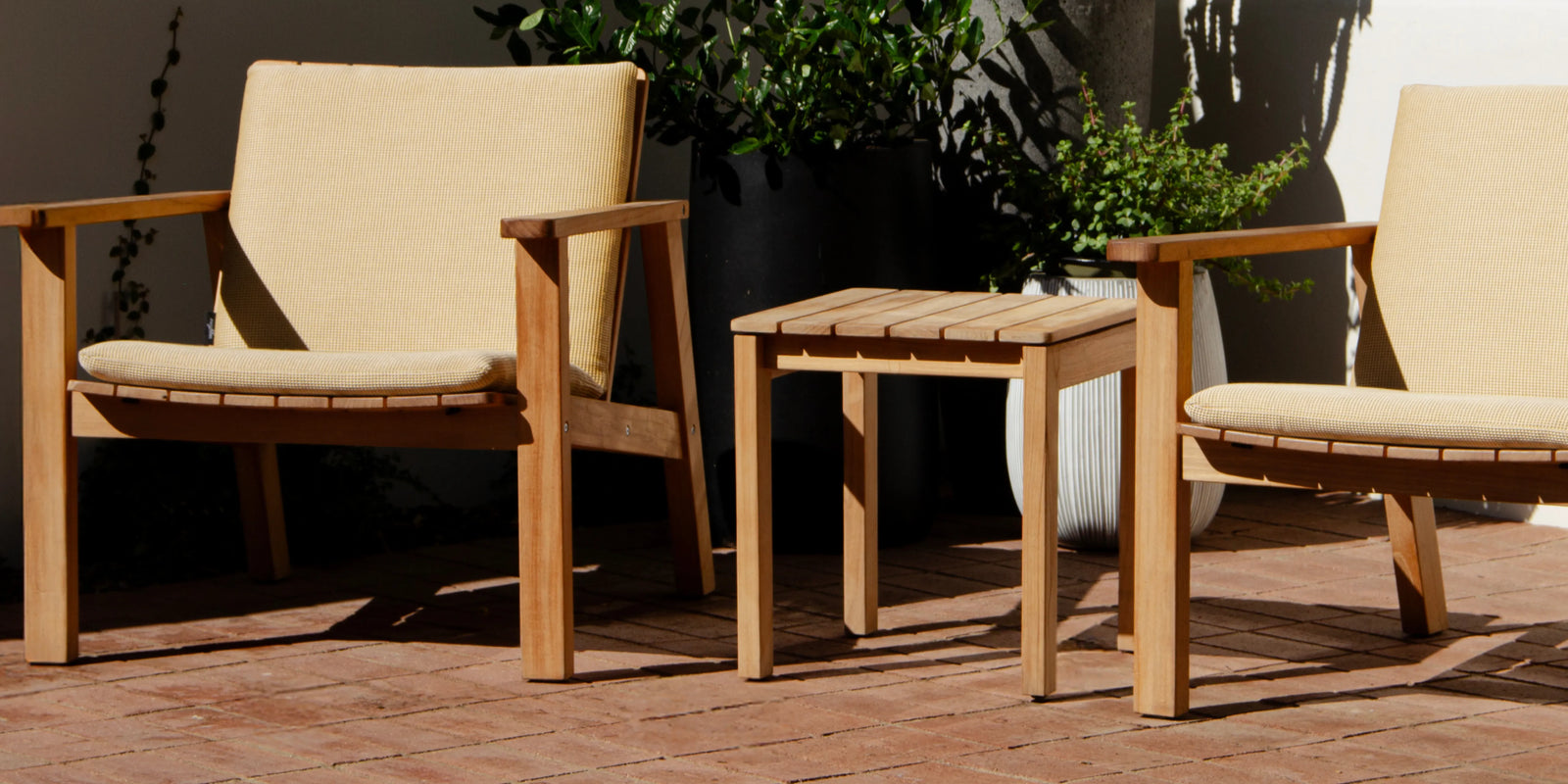 Neighbor Low Side Table in teak beside Low Chairs with cream cushions on a terracotta tile patio