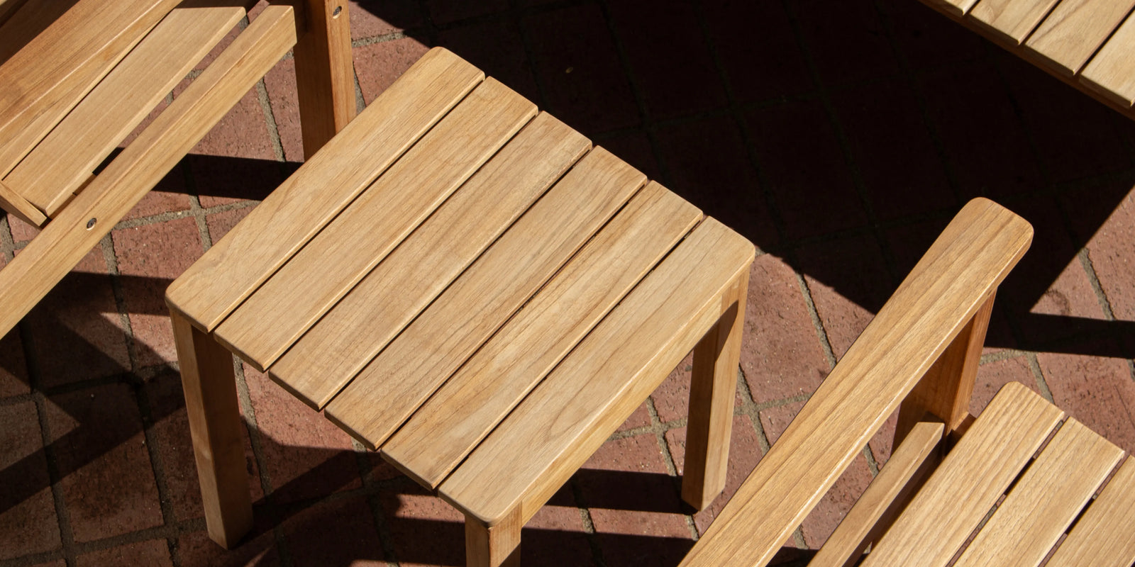 Overhead closeup of Neighbor Low Side Table teak top between Low Chair armrests on terracotta tile