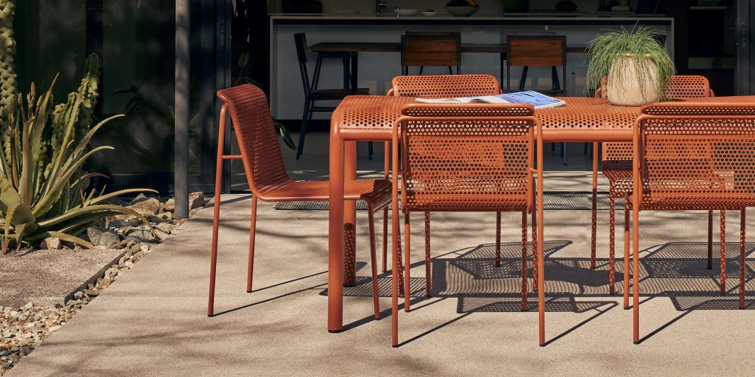 Neighbor Perf Dining Set with round table and perforated orange steel chairs on a grass lawn at dusk