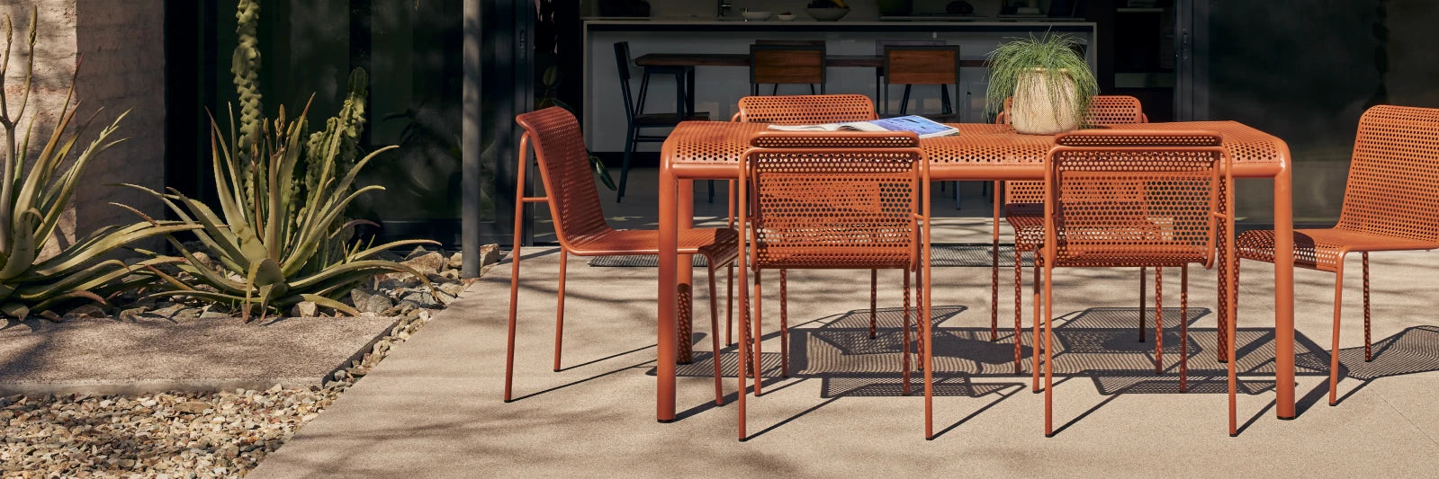 Neighbor Perf Dining Set with round table and perforated orange steel chairs on a grass lawn at dusk