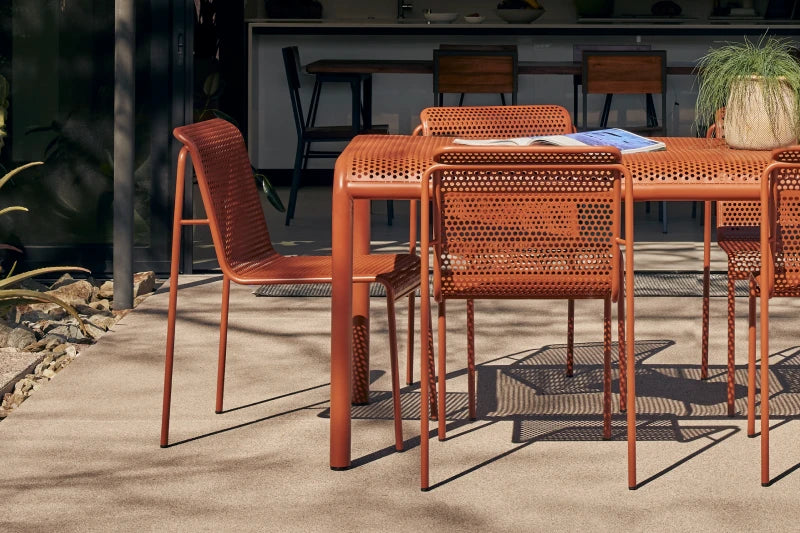 Neighbor Perf Dining Set with round table and perforated orange steel chairs on a grass lawn at dusk