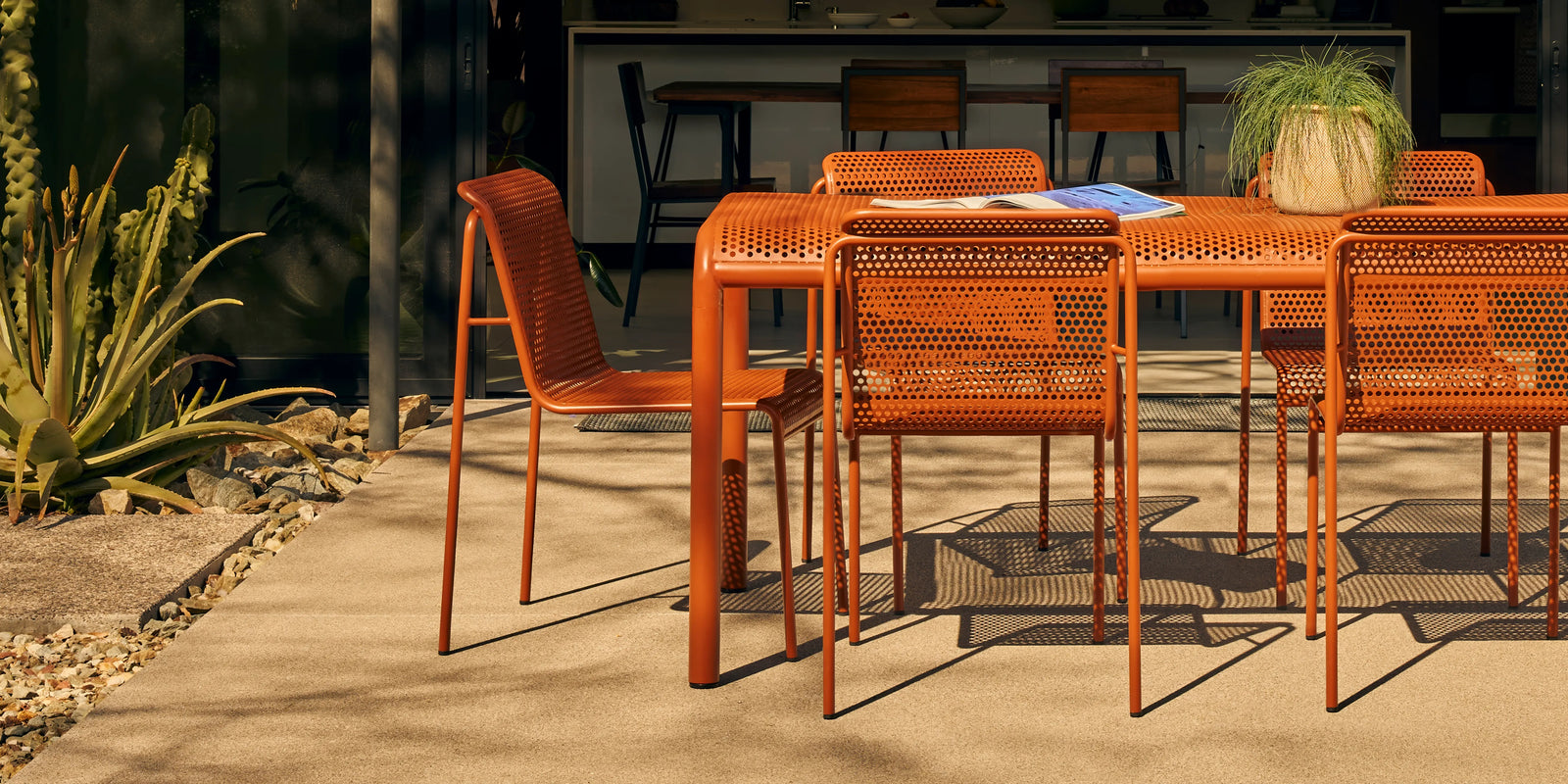Neighbor Perf Dining Set with round table and perforated orange steel chairs on a grass lawn at dusk
