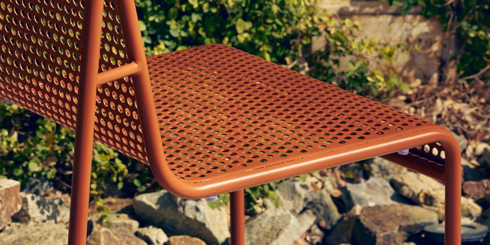 Closeup of Neighbor Perf Dining Set perforated orange chairs and teak-top table on lawn in low evening light