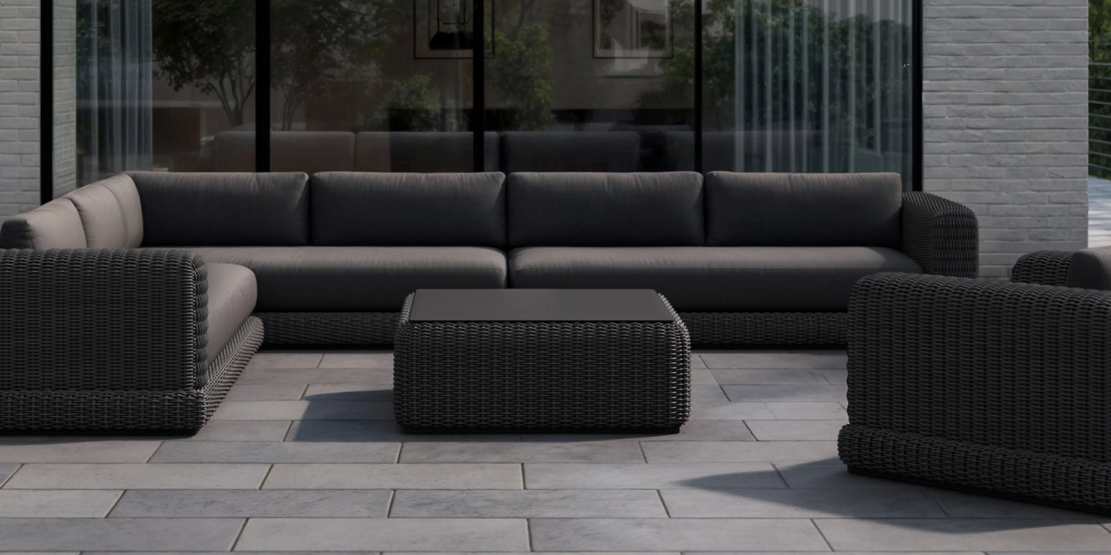 Neighbor Roundabout Sectional in dark wicker with charcoal cushions on a paved garden patio