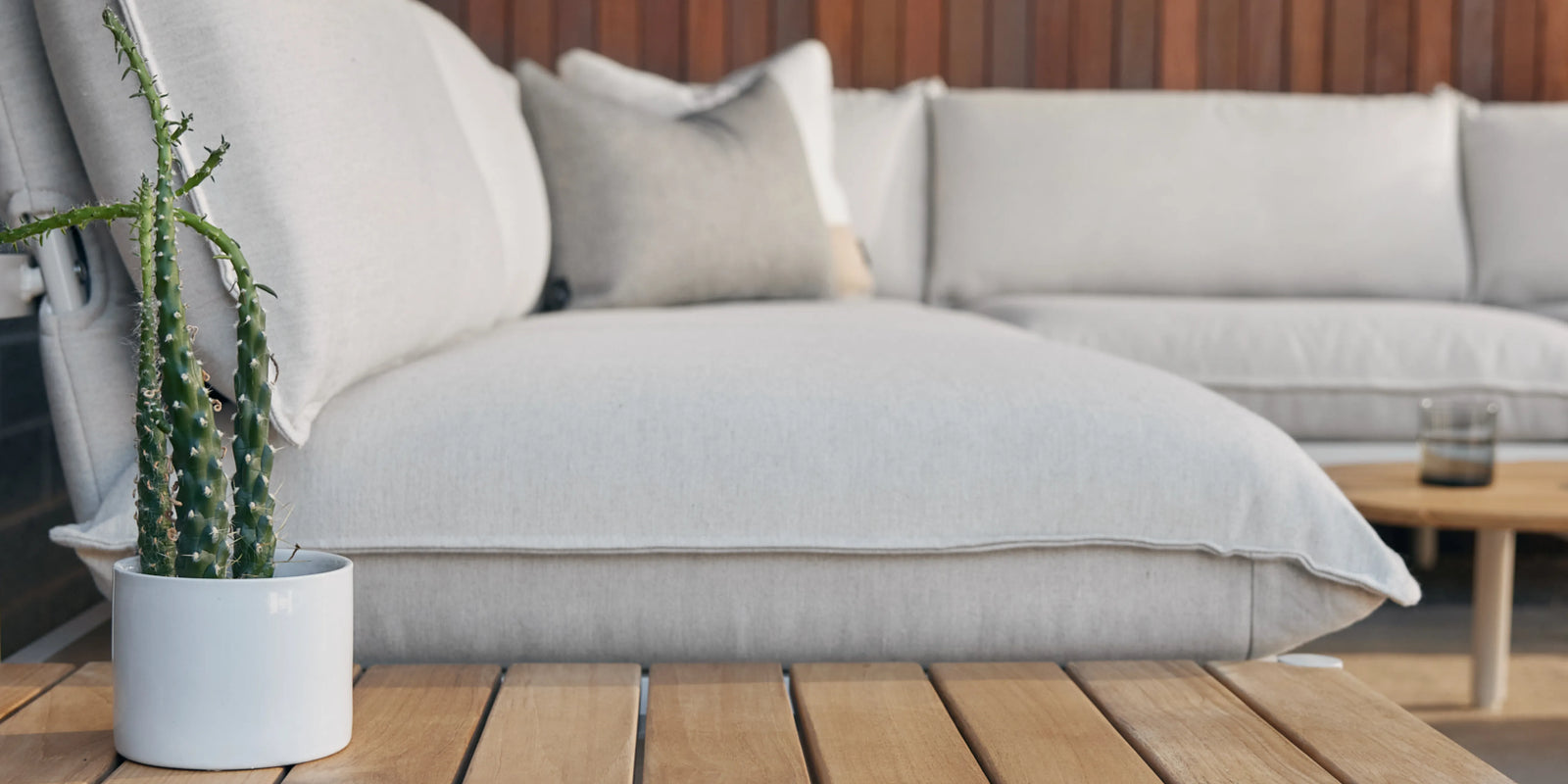 Closeup of Neighbor Terra End Table teak surface beside cream cushion sectional in outdoor light