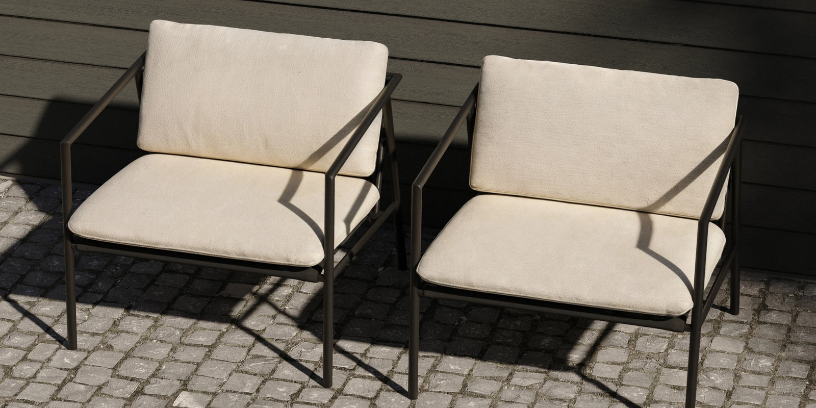 Two Neighbor Trase Chairs in cream cushion and Charcoal metal frame on cobblestone surface beside dark wood wall