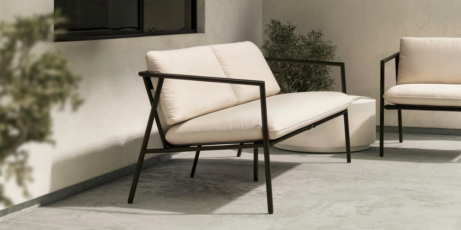 Closeup of Neighbor Trase Chair cream cushion and Charcoal powder-coated metal frame on cobblestone