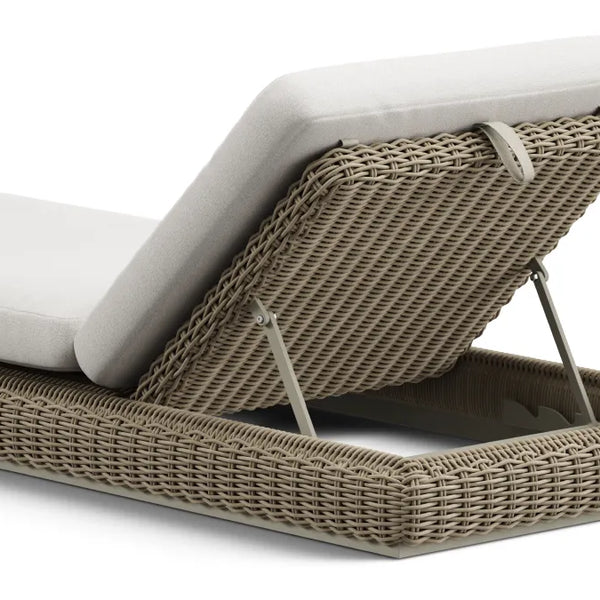 Close-up product photo of a Neighbor Roundabout Sun Lounger in taupe-gray resin wicker, viewed from behind to show the multi-position adjustable backrest mechanism with painted-steel ratchet hinges raising the cream cushion at a relaxed recline angle, isolated on a white background.