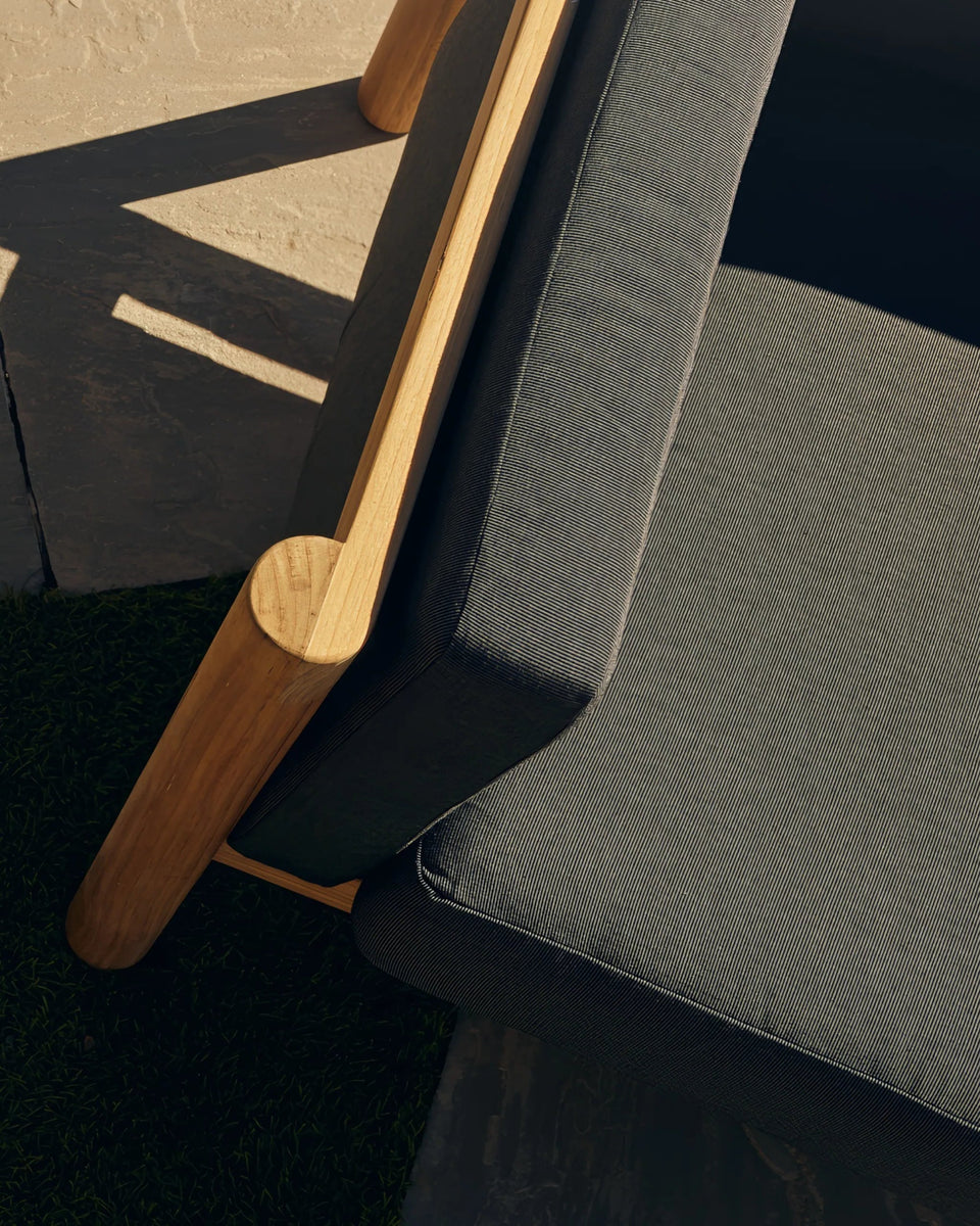 Overhead shot of a round concrete side table with a book and coffee cup, flanked by teak lounge chairs on a lawn