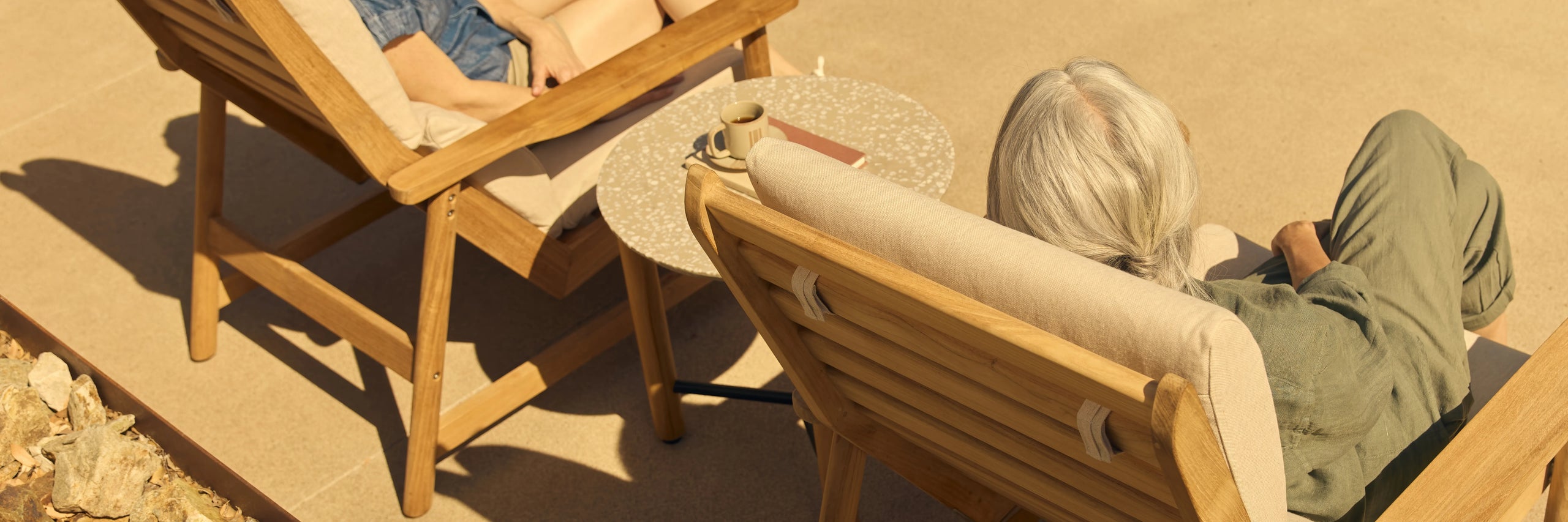 Aerial view of two people relaxing in teak sling lounge chairs on a warm sandy patio