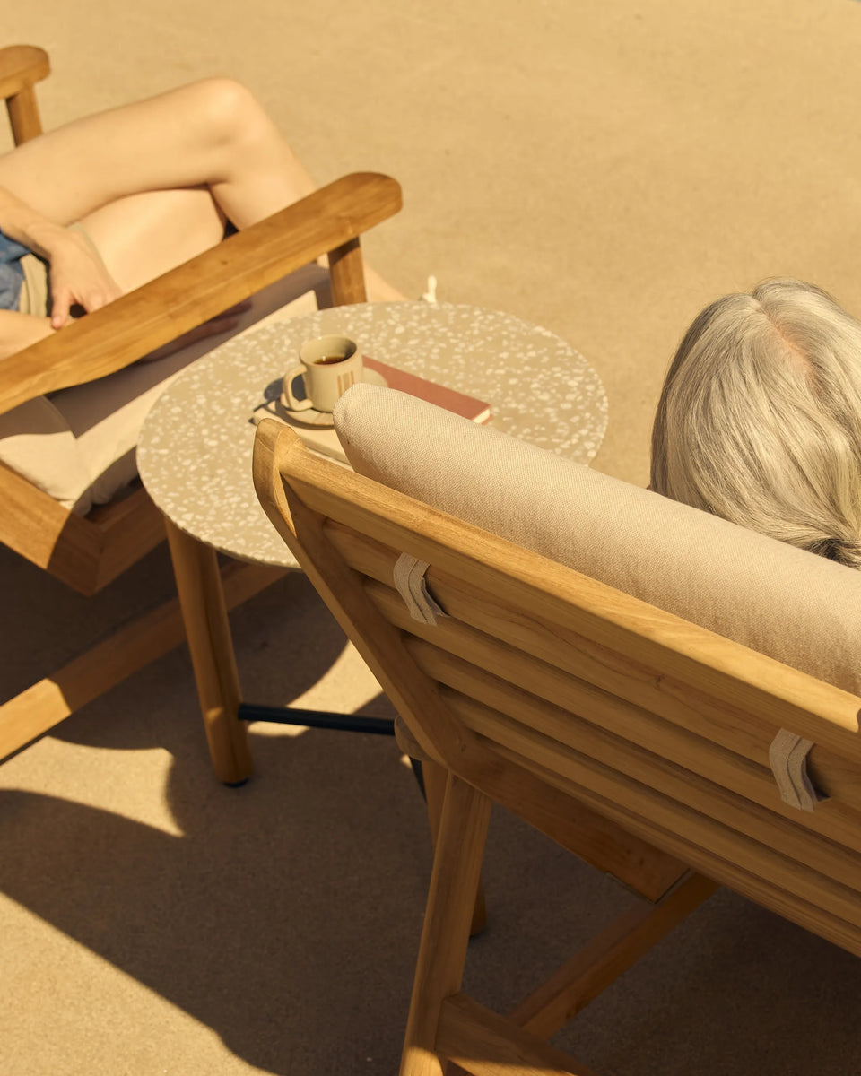 Aerial view of two people relaxing in teak sling lounge chairs on a warm sandy patio