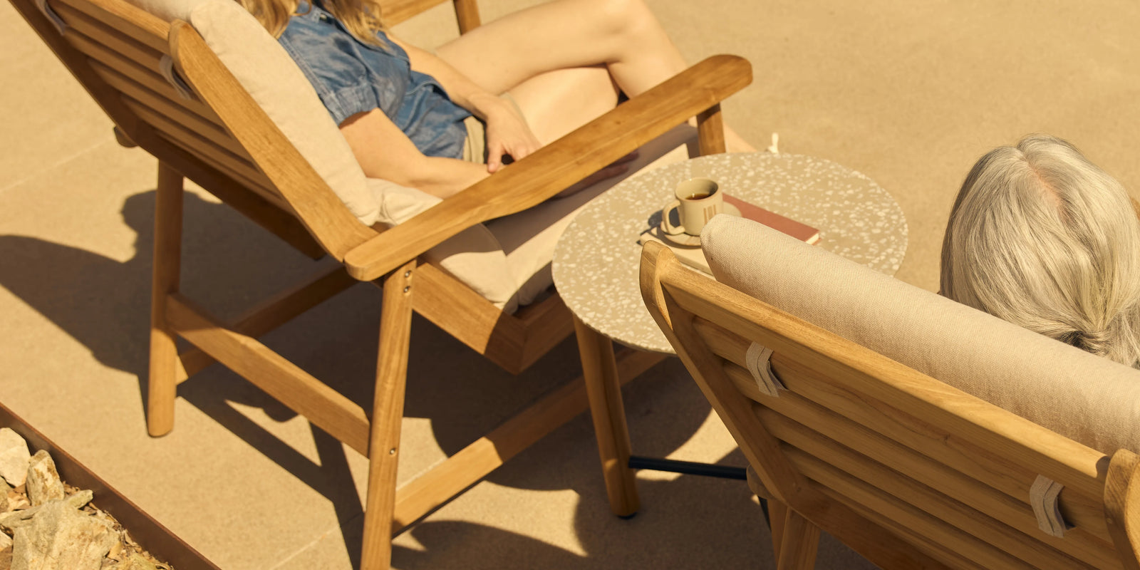 Aerial view of two people relaxing in teak sling lounge chairs on a warm sandy patio
