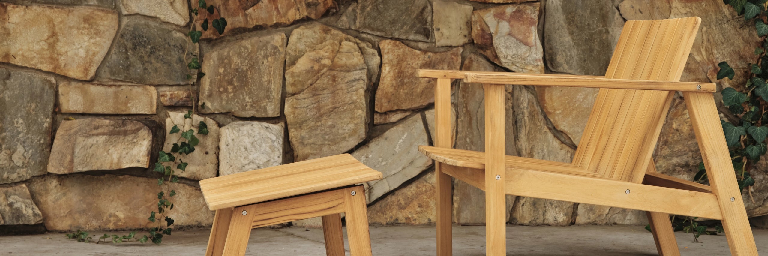 Teak adirondack-style lounge chair and matching footstool against a rustic stone wall