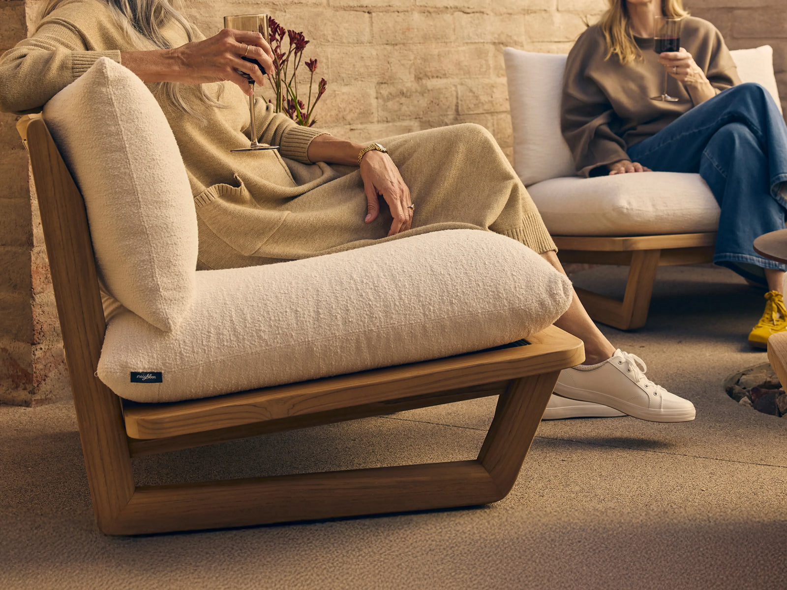 Close-up of a woman relaxing in a teak lounge chair with cream boucle cushions, holding a glass outdoors