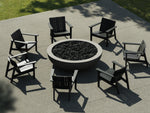 Neighbor Coupe Fire Table surrounded by six black Adirondack-style chairs on a concrete terrace with lawn beyond.