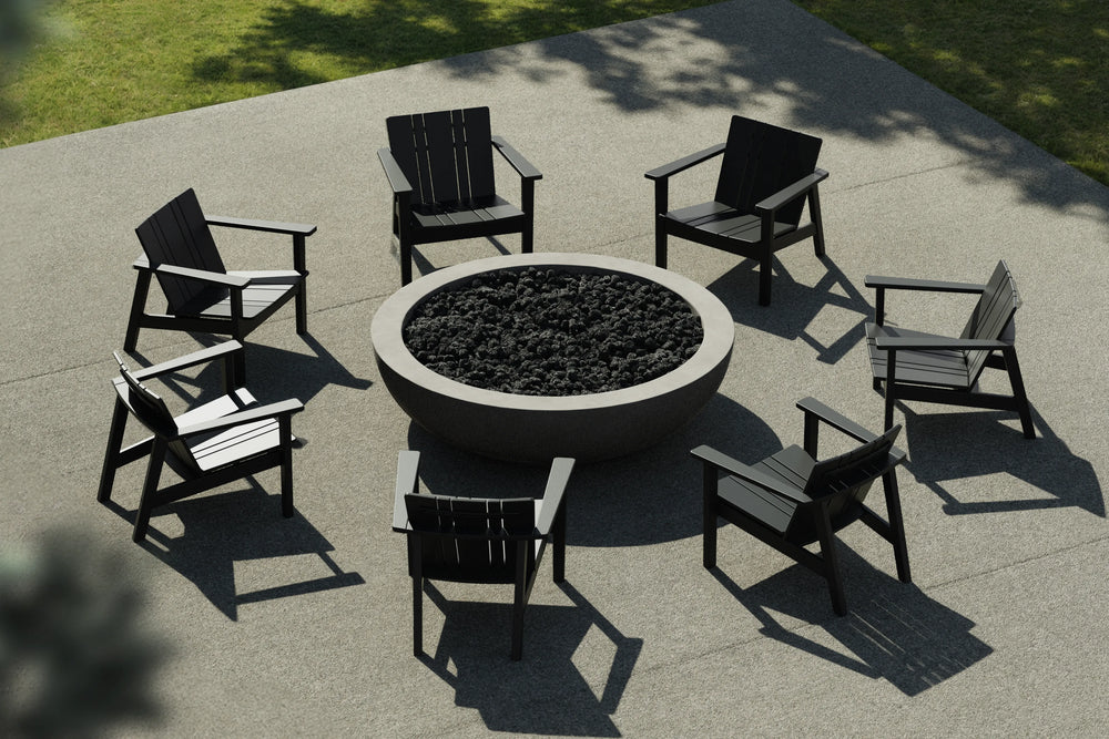 Neighbor Coupe Fire Table surrounded by six black Adirondack-style chairs on a concrete terrace with lawn beyond.